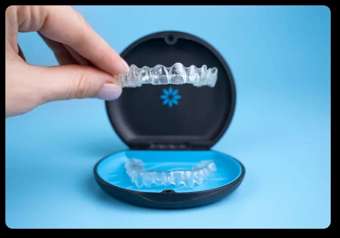 A hand lifting a clear aligner out of its round case